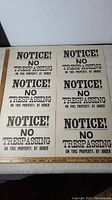 Photo showing six vintage No Trespassing signs arranged flat on a table, each with bold black text on a white background.