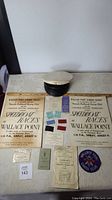 Full lot showing 2 posters, multiple ticket stubs and booklets, fabric patch, and a black and white nautical cap on a table.