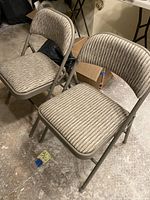 Two padded folding chairs with textured striped fabric upholstery and metal frames, positioned side by side.