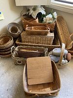 Photo showing multiple woven baskets piled together including rectangular, oval, and round shapes with a wooden lid basket on top.