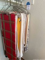 Photo of tablecloths hanging on hangers showing variety of colors and patterns including red plaid, white with motifs, solid yellow and neutral tones.