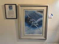 Overall view of the framed art print and the framed certificate of authenticity hung on the wall, showing the item presentation.