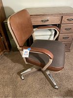 Side angle of the chair showing padded backrest, armrests and brown fabric seat cushion, chrome legs with casters visible.