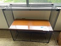 Side view of midcentury slatted shelving unit with wooden shelf and black metal frame, natural lighting near window.