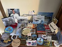 Display of military patches, pins, signed photos, postcards, and other memorabilia items arranged on a surface showcasing variety of collectible military-themed objects.