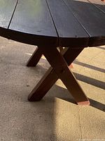View of the dark brown wooden table base with crossed legs on a concrete surface showing signs of weather wear and sturdy construction.