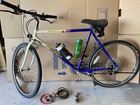 Full side profile of the bike showing frame, wheels, saddle, handlebars and included accessories (two water bottles, cable lock, quick-release skewers)