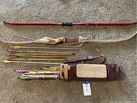 Two bows, multiple arrows, and a leather carrying quiver displayed on carpet