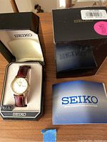 Full lot: vintage Seiko watch in open box with original price tag visible and instruction pamphlet on table.