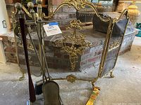 Full view of three-panel brass fireplace screen with tool set and matchbox on floor.