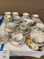 Full lot of 11 vintage cup and saucer sets spread on white towel showing floral patterns.