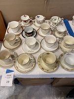 Overview of all 15 vintage teacup and saucer sets arranged on a table showing variety of floral and decorative patterns