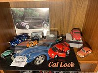 Display cabinet shelf with several Volkswagen Beetle toy cars in various colors and a black vintage Beetle poster in the background