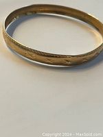 Angled view of gold bangle showing star pattern around exterior.