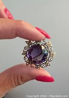 Hand-held view showing overall front appearance of brooch with amethyst center and surrounding pearls.