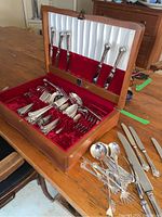 Full view of flatware set arranged in wooden canteen lined with red velvet and white satin under lid.