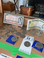 Photo showing two Canadian one-dollar bills, one two-dollar bill, and several scattered coins including some in blue holders.