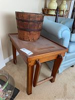 Full view of wooden utility cart with bucket on top, shows wood grain and cart legs with leather straps