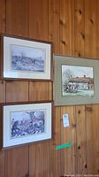 Three framed and matted horse prints hanging on a wood-paneled wall. Two are smaller with white mats, one larger with beige mat and gray frame.