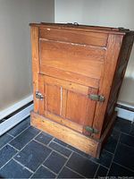 Front and side view of the oak ice chest showing rectangular form, wood grain, hinged lid, and front door with metal latches.