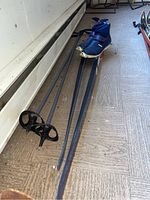 Blue pair of Karhu skis with poles and blue Karhu boots with velcro straps laid on floor
