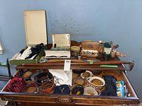 Dresser with open drawer showing rolled belts, shoelace pack, suspenders, cane atop