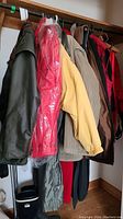 Hanging men's winter coats and jackets including fleece, corduroy, rain jacket, and insulated styles in various colors including dark olive, red, tan, black, and red.