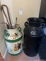 Front view of both milk cans side by side with canes inside painted can