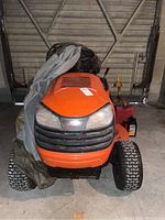 Front view of orange Ariens riding mower showing hood, headlights and front wheels