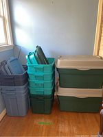 Side view of gray Rubbermaid storage bins stacked with lids, teal Rubbermaid bins stacked with lids, and two large Roughneck bins stacked