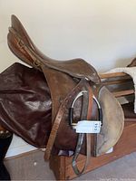 Side view of brown leather Sprenger saddle with stirrups and part of Sherpa cover.