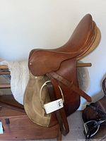 Left-side view of saddle on rack showing leather flaps, suede knee roll and attached stirrup iron with leather stirrup leather.