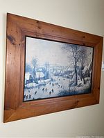 Frontal view of wood framed print showing winter ice rink scene with skaters and snowy houses.