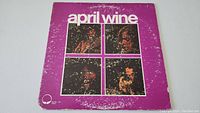 Full front cover photo of the April Wine vinyl album showing four photos of band members on purple background with visible wear and scuffing.