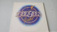 Front cover of the Bee Gees Greatest Hits vinyl album showing the logo design in gold and blue tones on a white background.