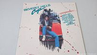 Front cover of Beverly Hills Cop soundtrack vinyl record showing man sitting on hood of red car with artist names.