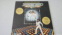 Front cover of the Saturday Night Fever soundtrack vinyl album with main illustration and gold promotional text.
