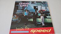 Front cover of Stray Cats Built For Speed album showing band members and vintage cars.
