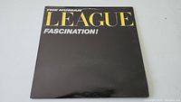Front cover of The Human League 'Fascination!' vinyl record sleeve showing the album title in yellow and white text on a black background.