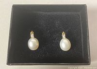 Full view of the pair of drop earrings with pearls and diamonds in a black box.