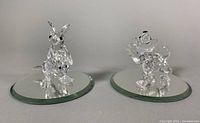 Two Swarovski Austrian crystal figurines, kangaroo and dog, displayed side by side on circular beveled mirrored bases reflecting light, showing clear detail and faceting.