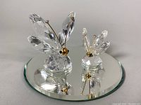 Front view of both large and small Swarovski crystal butterfly figurines positioned on the round beveled mirrored base.