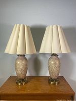 Pair of vintage table lamps with splattered colored glass bodies, brass bases, and cream pleated shades side by side