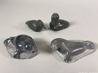 Four vintage Inuit soapstone carvings including birds and seals, arranged on a white surface to show front and sides.