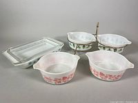 Front view of all items: lasagna pan with lid, Pink Gooseberry and Green Blue Leaves casserole dishes on brass holder