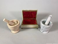 Front view of two marble mortar and pestle sets alongside the open lined brass claw footed jewelry box showing red velvet interior.