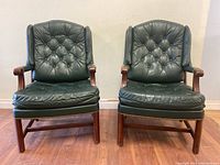 Front view of both chairs showing button-tufted backs, seat cushions, wood frames and nailhead trim
