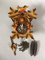 Full view of cuckoo clock with two weights, pendulum, and chain displayed on a white background.
