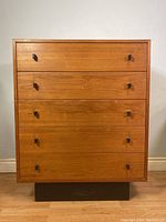 Front view of dresser showing teak veneer finish and five drawers in light wood tone.