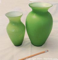 Two green translucent glass vases shown on light background with pencil for scale, highlighting differing sizes and matte finish.